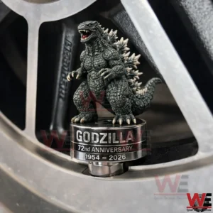 Godzilla miniature figure on a metallic tire valve cap base reading Godzilla 72nd Anniversary 1954 2026 inside a car wheel rim close up!