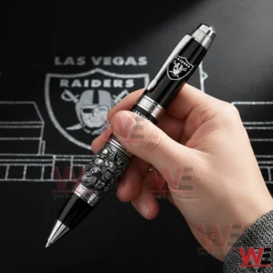 Las Vegas Raiders 66th Anniversary 1960-2026 Pen 3 Hand holding a black and silver Las Vegas Raiders sixty sixth anniversary ballpoint pen with Raiders logo and detailed football player artwork against a Raiders themed background.