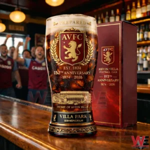 A decorative Aston Villa beer glass with detailed crest and anniversary artwork standing on a bar with football fans celebrating behind it!