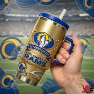 A hand holding a gold Los Angeles Rams insulated tumbler with blue handle and straw showing 90th anniversary 1936 to 2026 design with Rams logo and football stadium background!