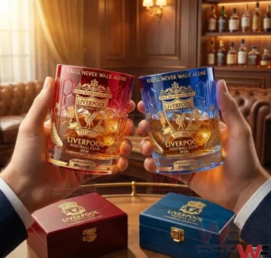 Liverpool Football Club 2026 Commemorative Whiskey Glass 8 Two hands holding red and blue Liverpool Football Club 2026 commemorative whiskey glasses above premium gift boxes in an elegant bar setting!