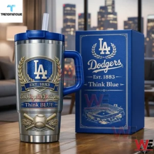 Silver Los Angeles Dodgers tumbler with blue handle and straw next to a matching gift box showing LA shield laurel wreath est 1883 think blue text baseball and crossed bats with a city skyline background