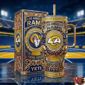 A Los Angeles Rams themed insulated tumbler with intricate patterns and team logo stands next to its matching box on a reflective surface inside a football arena!