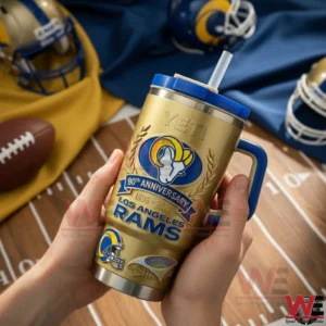 Hands holding a gold Los Angeles Rams 90th anniversary insulated tumbler with blue handle and straw on a football themed background.