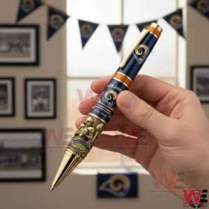 Los Angeles Rams 90 Years 1936-2026 Pen 3 Hand holding a Los Angeles Rams anniversary pen with gold trim and engraved football design with team banners and framed photos in the background!