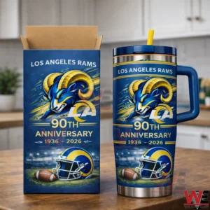 Blue Los Angeles Rams tumbler with navy lid and yellow straw on a wooden counter next to a matching open top box showing a ram head graphic and Ninety Th Anniversary Nineteen Thirty Six to Two Thousand Twenty Six design in a kitchen.