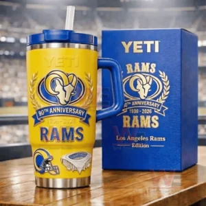 Yellow and blue YETI Rams 90th Anniversary tumbler next to a blue Rams themed gift box on a table with a blurred stadium behind!