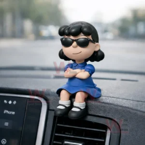Cartoon girl figurine with black hair and sunglasses wearing a blue dress sitting with crossed arms on a car dashboard above an air vent with a blurred road background!