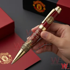 Hand holding a Manchester United red and gold anniversary pen with engraved club emblem and premium finish!