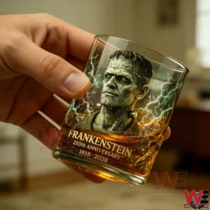 A hand holds a Frankenstein themed whiskey glass with electric lightning design and golden whiskey inside!