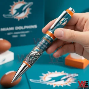 Miami Dolphins 60th Anniversary 1966-2026 Pen 6 Hand holding a teal and orange Miami Dolphins sixtieth anniversary ballpoint pen with team logo anniversary text and dolphin artwork against a Miami Dolphins themed background.