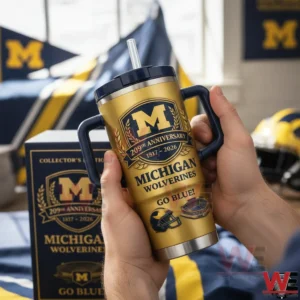 Hands holding a gold Michigan Wolverines anniversary insulated tumbler with handles and straw with a matching collector edition box and Michigan themed decor in the background!