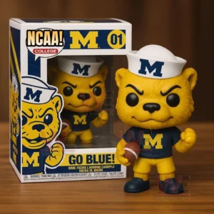 Yellow Michigan Wolverines mascot vinyl figure with an M shirt and sailor hat holding a football next to a NCAA Michigan collectible box on a wooden table.