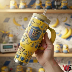 Hand holding a yellow Minions themed tumbler with banana handle clear straw stainless steel base and detailed character illustrations in a themed background!