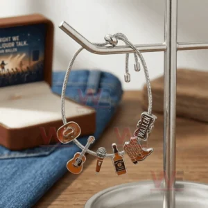 Adjustable charm bracelet on a metal stand with cowboy hat guitar microphone whiskey bottle cowboy boots and Wallen name charms near a gift box and denim.