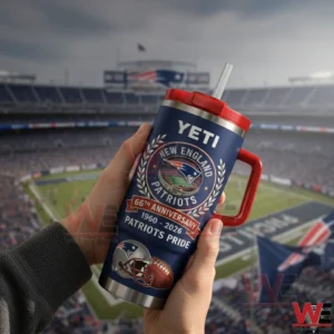 Hands holding a navy New England Patriots 66th anniversary insulated tumbler with red handle and straw in front of a football stadium.