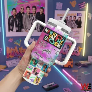 Hand holding a colorful New Kids On The Block tumbler with a white handle and straw in front of retro posters and neon lights!