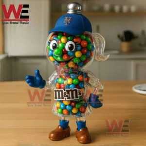 Clear character candy jar filled with colorful chocolate candies wearing a New York Mets cap on a wooden table with a kitchen background.