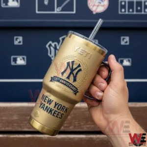 Hand holding a gold New York Yankees one hundred twenty fifth anniversary tumbler with handle and straw against a baseball dugout themed background!