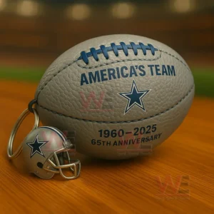 Gray and blue Cowboys football keychain with star logo Americas Team text 1960 2025 65th anniversary and a small helmet charm on a wooden table with stadium blur!