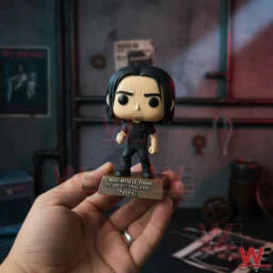 A hand holding a collectible figure of Trent Reznor with dark hair black clothing and a microphone standing on a themed display base in an industrial setting!