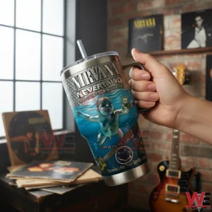 Hand holding a Nirvana Nevermind 35th anniversary stainless steel tumbler with handle and straw featuring an underwater baby illustration in a cozy room with records posters and guitars!