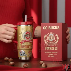 Person holding Ohio State Buckeyes one hundred thirty fifth anniversary gold tumbler with red handle and straw beside a red Go Bucks collector box on a table with buckeye nuts!