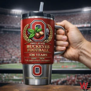 Ohio State Buckeyes 136th Anniversary 1890-2026 Tumbler 4 Hand holding a red Ohio State Buckeyes Football insulated tumbler with handle straw 136 Years design and 1890 2026 text in front of a blurred stadium scene!