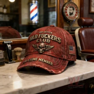 Distressed red baseball cap with embroidered skull wings emblem and bold text on a marble counter in a vintage barbershop with barber tools and a striped barber pole in the background!