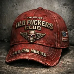 Close up of a distressed red baseball cap with embroidered skull wings emblem and bold text featuring a frayed brim and an American flag patch against a textured gray concrete background!