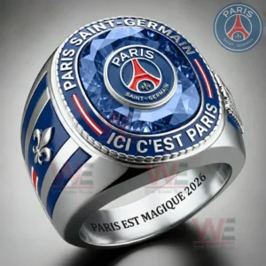 A silver Paris Saint Germain ring with a blue gemstone top featuring the PSG crest and engraved text Paris Saint Germain and Ici Cest Paris with side fleur de lis details and inner band text Paris Est Magique 2026!