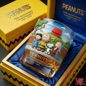 A Peanuts seventy fifth anniversary commemorative whiskey glass with cartoon characters artwork amber whiskey and a luxury yellow presentation box!