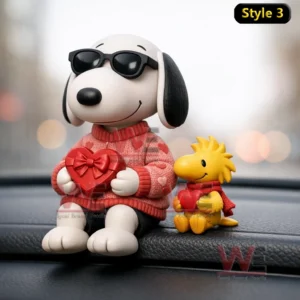 White dog figurine wearing sunglasses and a red sweater holding a heart gift next to a small yellow bird on a car dashboard.