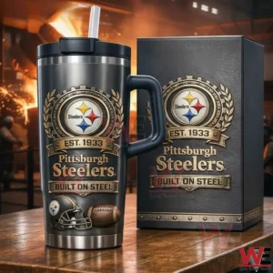 Dark Pittsburgh Steelers tumbler with handle lid and straw on a wooden table next to a matching collector box featuring the Steelers logo Est Nineteen Thirty Three and Built On Steel design in an industrial steelwork setting.