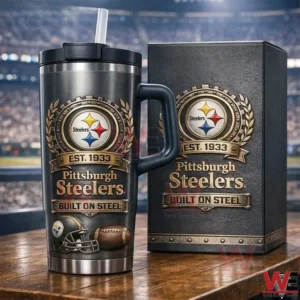 Dark Pittsburgh Steelers tumbler with handle lid and straw on a wooden table next to a matching collector box featuring the Steelers logo Est Nineteen Thirty Three and Built On Steel design with a stadium background.