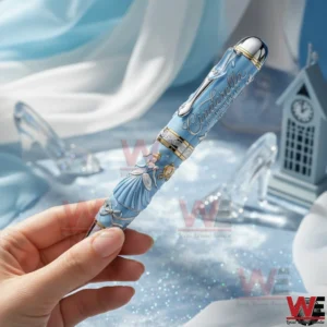 Hand holding a Cinderella commemorative pen with blue fairytale artwork silver accents and a dreamy sparkling background with glass slipper decorations.