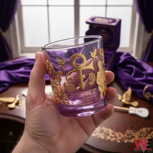 Hand holding a Prince memorial anniversary whiskey glass with gold detailing and purple tones!