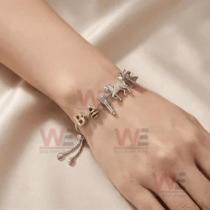 Adjustable silver tone charm bracelet on a wrist with letter B bee microphone unicorn cozy text and crystal charms in soft light.