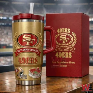 Gold San Francisco 49ers insulated tumbler with red handle and straw placed next to a red gift box showing 80th anniversary 1946 to 2026 branding on a wooden table with stadium background!