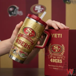 Hands holding a gold San Francisco 49ers eightieth anniversary insulated tumbler with red handle and straw lid beside a matching red commemorative gift box on a sports themed background!