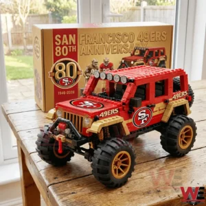 A red and gold off road truck building block model with large wheels and team logos displayed on a wooden table with an anniversary box!