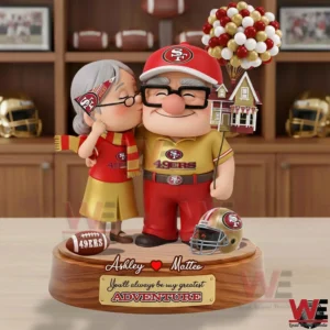 A detailed couple figurine in San Francisco football themed clothing standing closely together with balloons a helmet and a football on a decorative base!