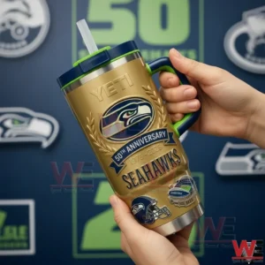 Seattle Seahawks 12th Man Go Hawks 50th Anniversary 1976-2026 Yeti Tumbler 5 Two hands holding a gold Seattle Seahawks fiftieth anniversary insulated tumbler with navy and green handle lid and straw against a blurred team logo background!