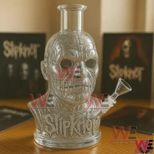 Clear glass masked face water pipe with Slipknot logo on the base displayed on a wooden table with Slipknot albums in the background!