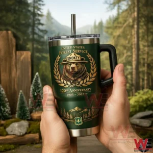 Hands holding a dark green United States Forest Service Smokey anniversary tumbler with handle and straw with a mountain forest landscape in the background!