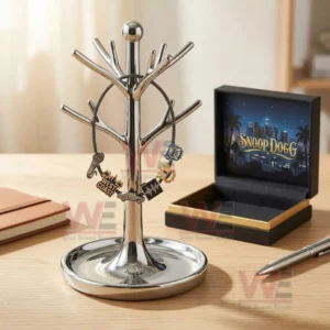 Silver adjustable charm bracelet with microphone West Coast lowrider audio waveform crown and bulldog charms hanging on a jewelry tree stand next to an open Snoop Dogg city skyline gift box.
