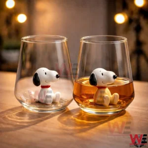 Two clear glass cups on a wooden surface with small white dog figurines inside one filled with amber liquid and one empty!
