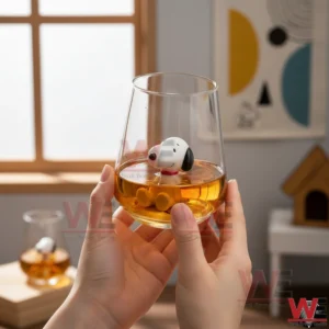 Hands holding a clear glass cup with a small white dog figurine inside amber liquid in a softly lit room!