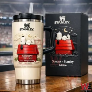 Cream Stanley tumbler with Snoopy anniversary design and straw next to a matching Snoopy Stanley Edition gift box on a wooden surface!