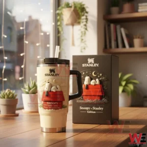 Snoopy Sleep on a Roof 75Th Anniversary Stanley Tumbler Cup 4 Stanley tumbler with Snoopy anniversary artwork and straw next to a matching gift box on a wooden table in a bright cozy room!